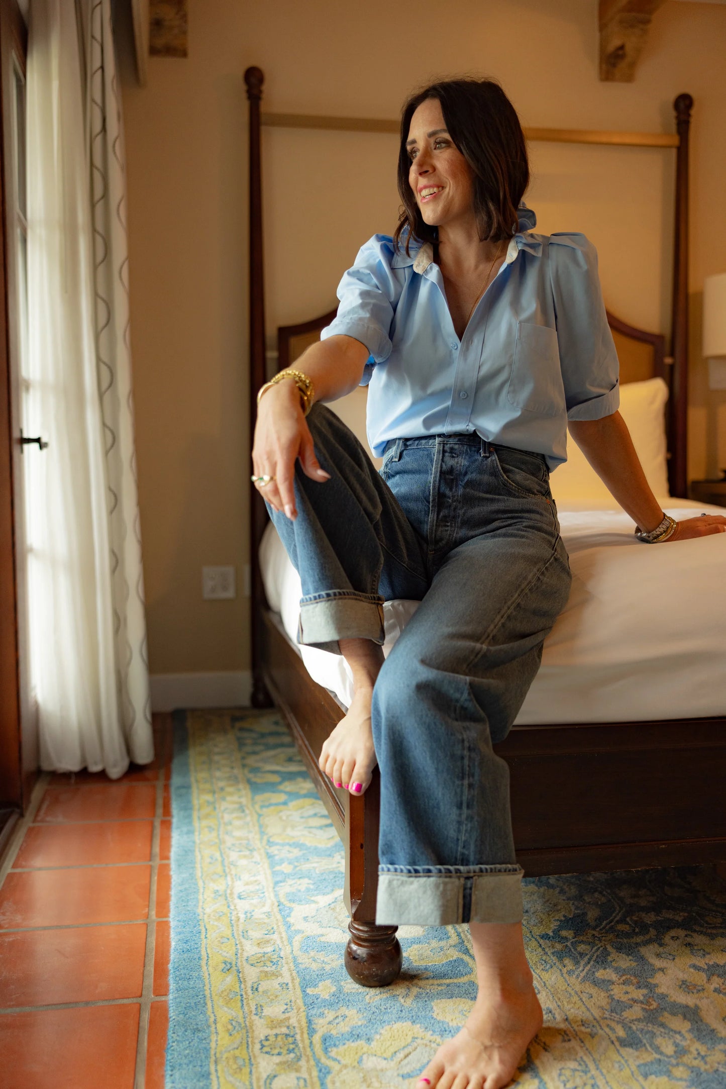 KMJ Bonita shirt in light blue with ruffle collar paired with casual shorts, styled by designer Kate in a serene hotel room setting in California.