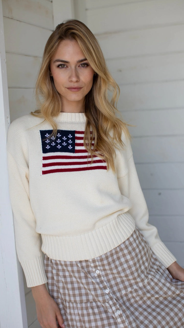 The Marea Flag Sweater in ivory styled with a gingham skirt for a charming, heritage-inspired outfit.