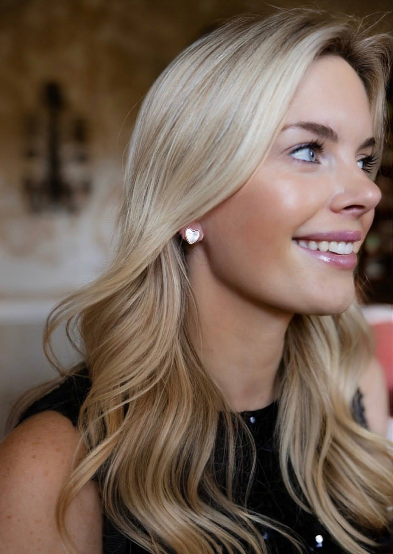 Woman wearing Darby Clark 18k gold plated mother of pearl heart stud earrings.