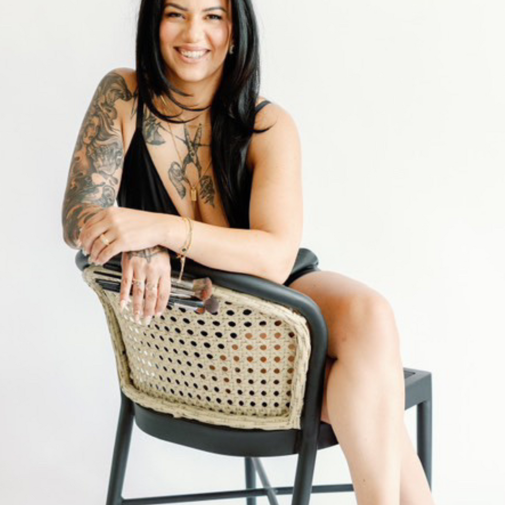 
                      
                        Nadia sitting in her studio chair, looking at the camera, ready to share her makeup artistry expertise in the upcoming workshop.
                      
                    