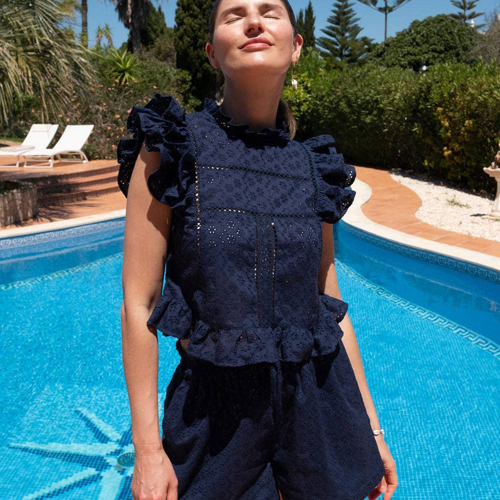 
                      
                        Model standing poolside in the Olivia shorts and Sasha top matching set in navy eyelet, styled for summer.
                      
                    