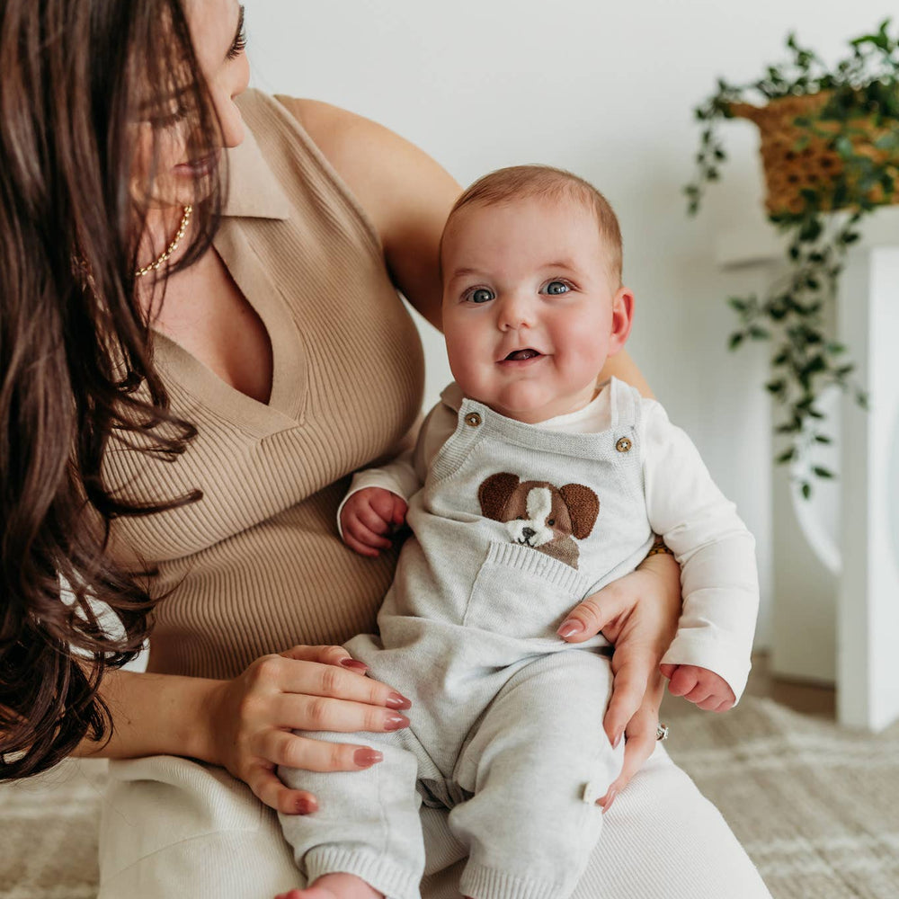 
                      
                        Seated baby in mom's lap wearing sweater knit Puppy Overall Set by Viverano, with cozy organic fabric and playful design
                      
                    