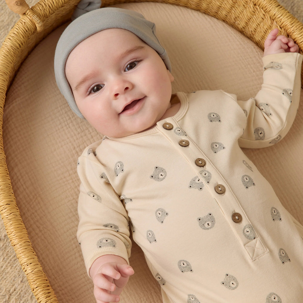 Baby in Quincy Mae long sleeve bears jumpsuit, organic cotton one-piece, looking up from bassinet with cozy comfort.