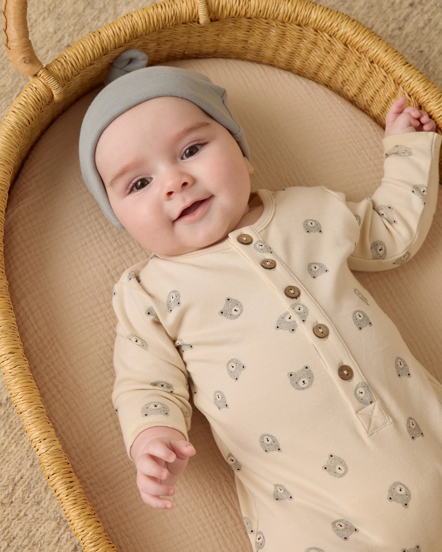 Baby in Quincy Mae long sleeve bears jumpsuit, organic cotton one-piece, looking up from bassinet with cozy comfort.
