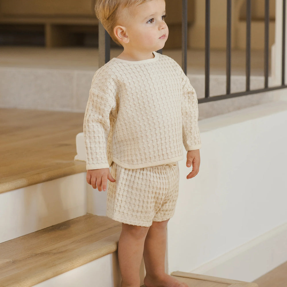 Baby boy wearing Quincy Mae Flynn Set in natural chunky waffle knit, standing to show breathable top and shorts designed for everyday comfort and play.