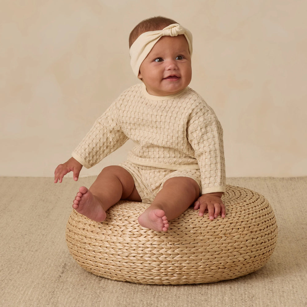
                      
                        Baby girl in Quincy Mae Flynn Set natural chunky waffle knit, sitting to highlight cozy, breathable design and relaxed fit.
                      
                    