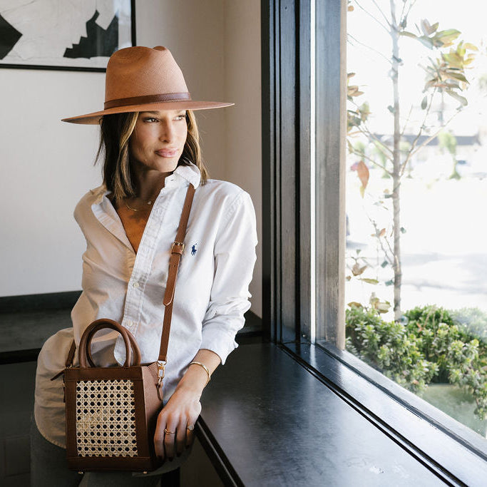 Side view of rattan bag worn crossbody showing structured shape and gold feet.