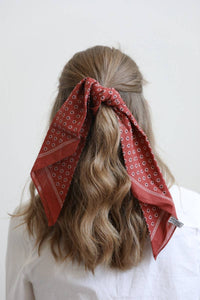 Person with red patterned bandana in hair against a white background