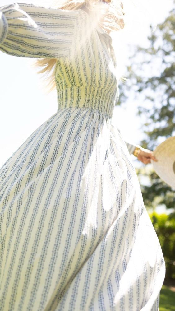Woman twirling in the Sable Dress in floral stripe with her sun hat, capturing the playful movement of the bias-cut maxi dress.