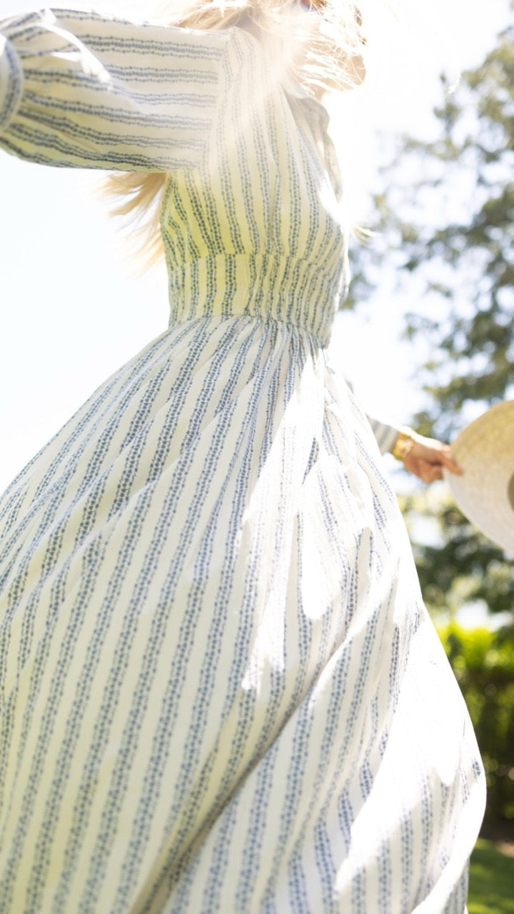 Woman twirling in the Sable Dress in floral stripe with her sun hat, capturing the playful movement of the bias-cut maxi dress.
