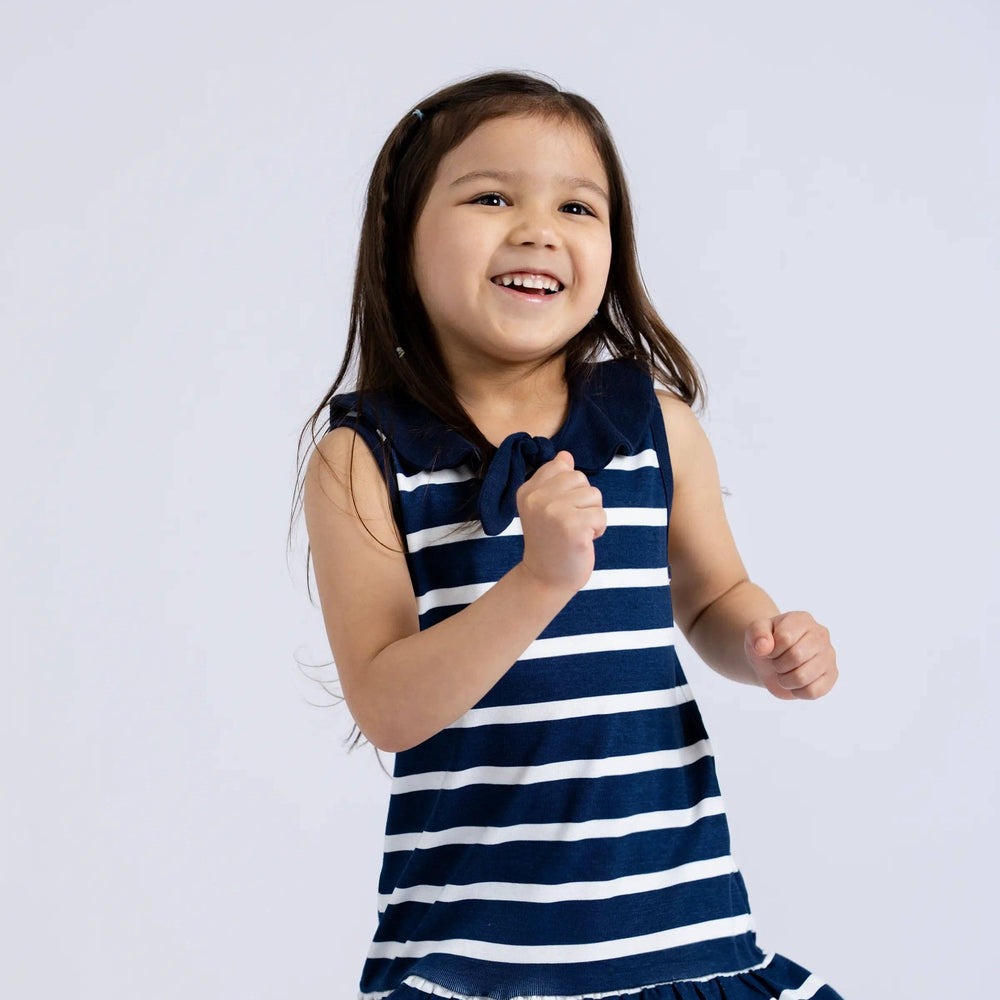 Girl twirling in Sailor Dress with navy stripes in a light-filled studio, showing full movement of the dress