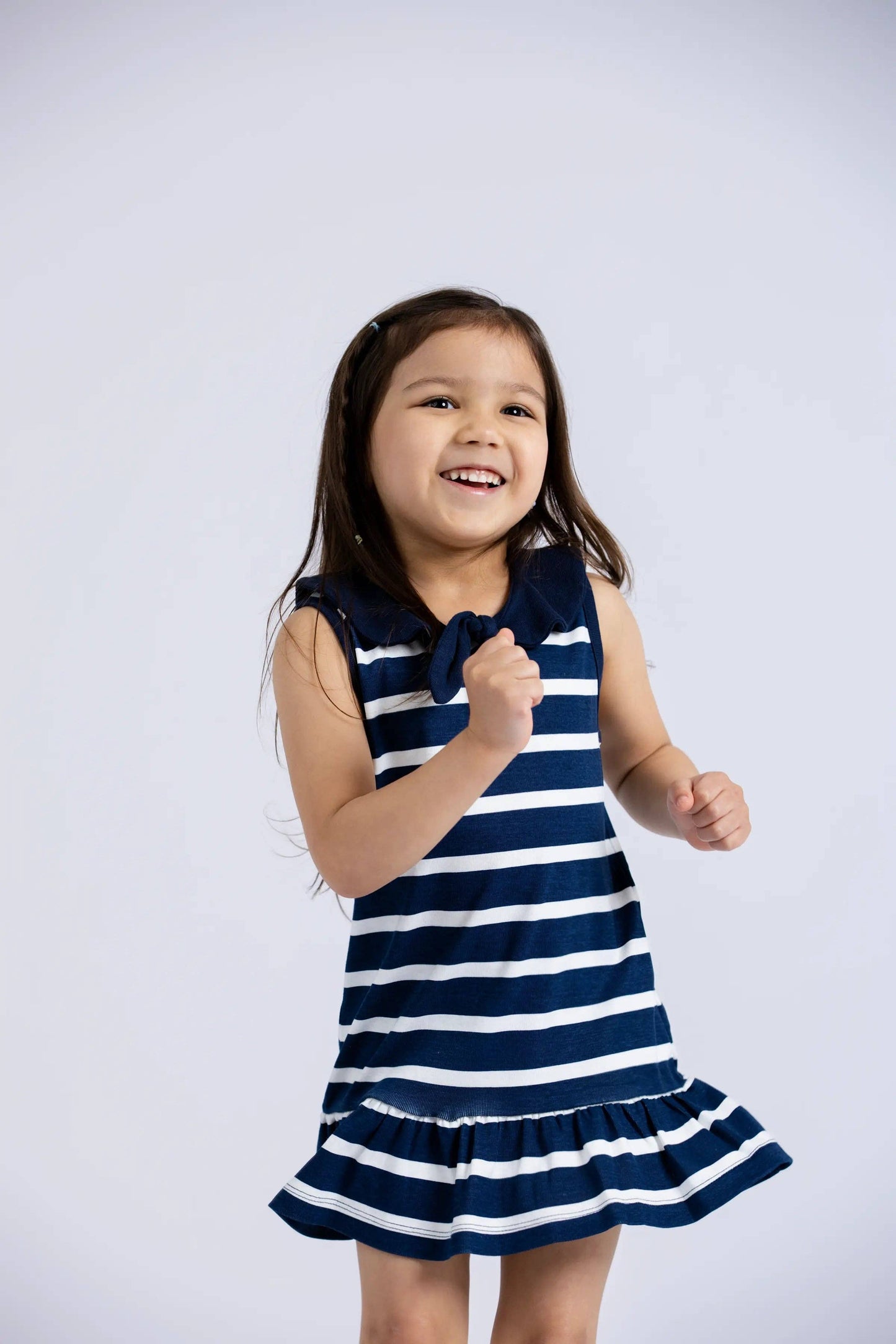 Girl twirling in Sailor Dress with navy stripes in a light-filled studio, showing full movement of the dress