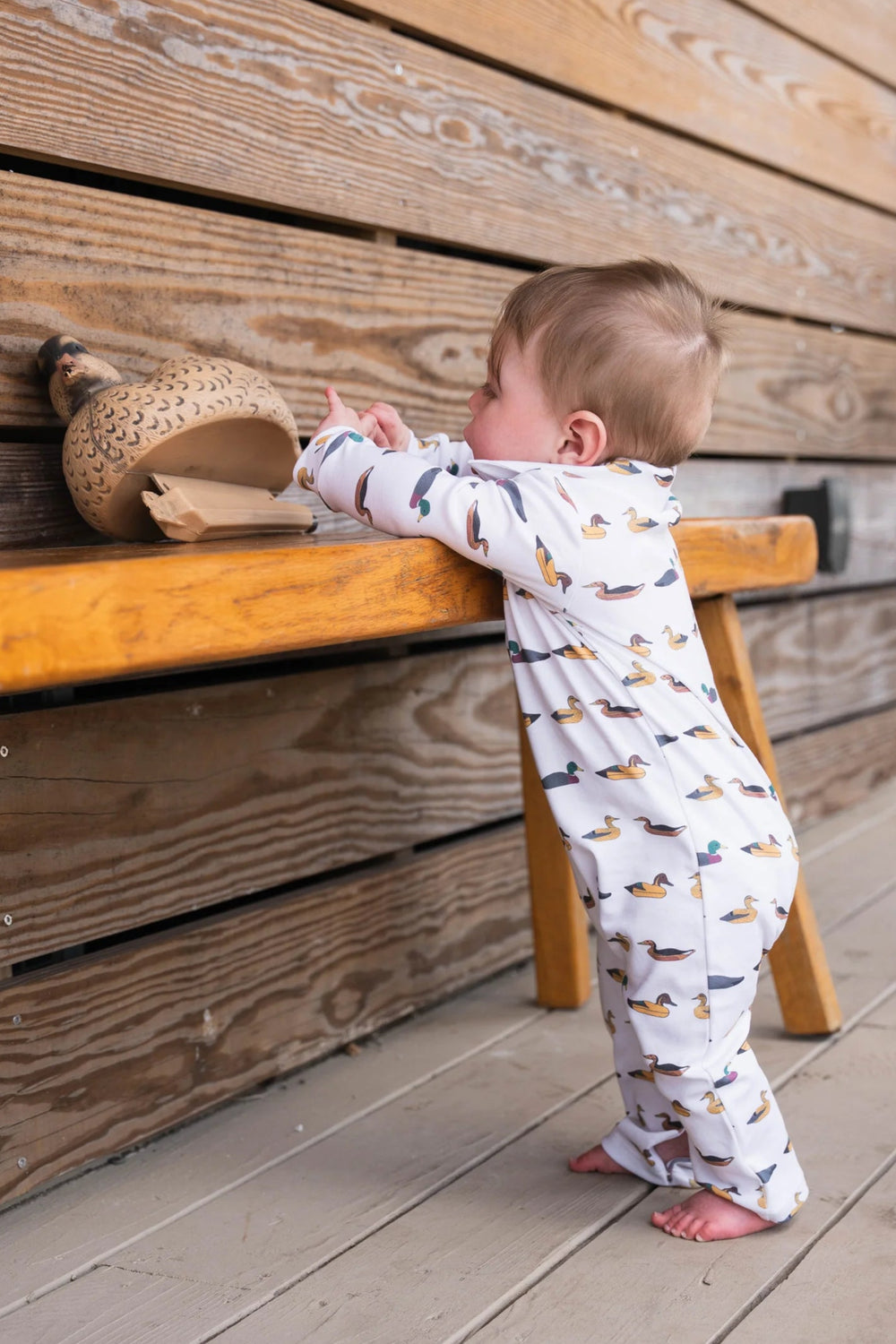 Baby in SBC Signature Polo Long-Sleeve Romper standing with a duck decoy, showcasing durable, comfortable design perfect for active babies.