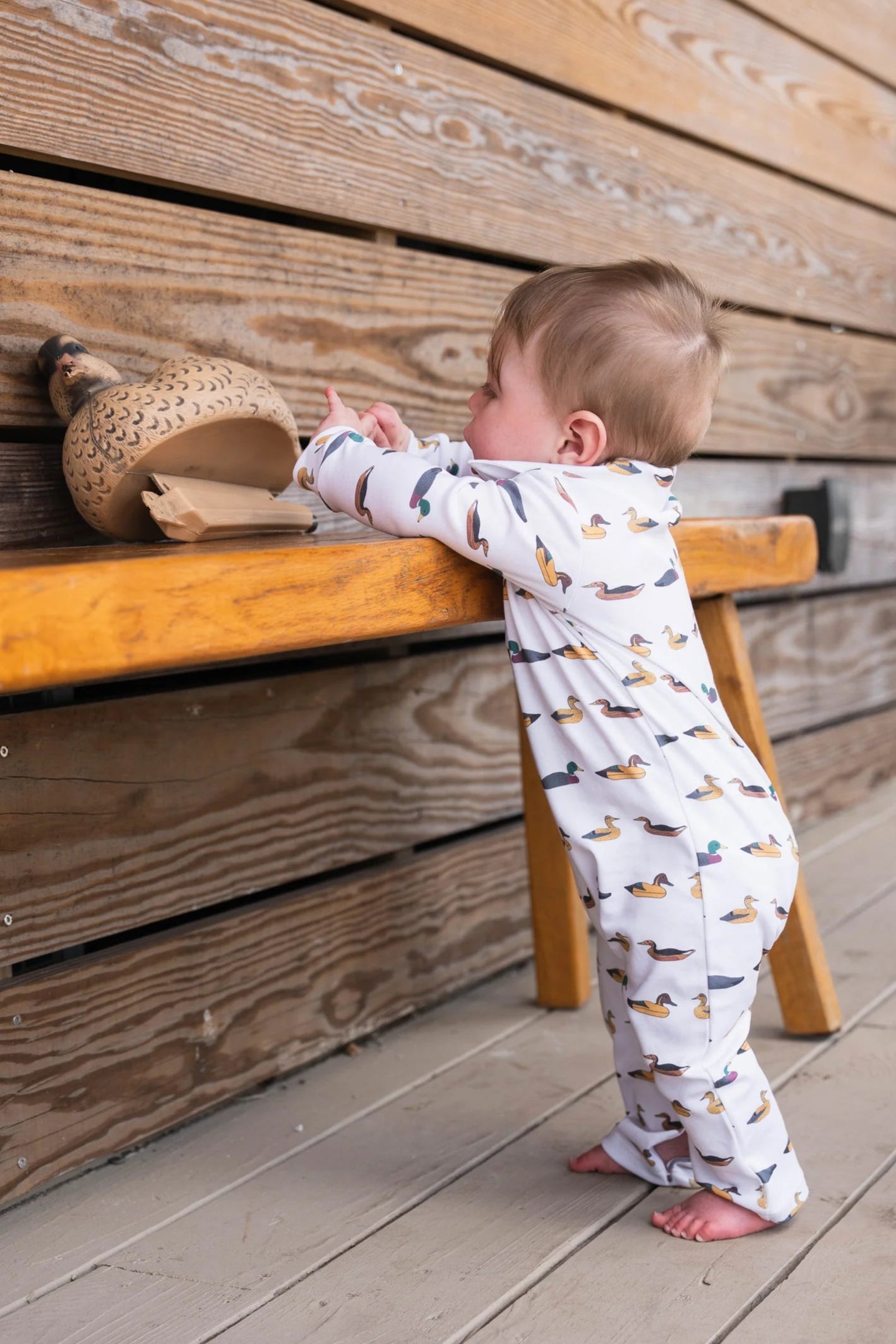 Baby in SBC Signature Polo Long-Sleeve Romper standing with a duck decoy, showcasing durable, comfortable design perfect for active babies.