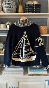 Navy varsity cardigan hanging against a nautical bookcase, showcasing the knitted sailboat design on the back.