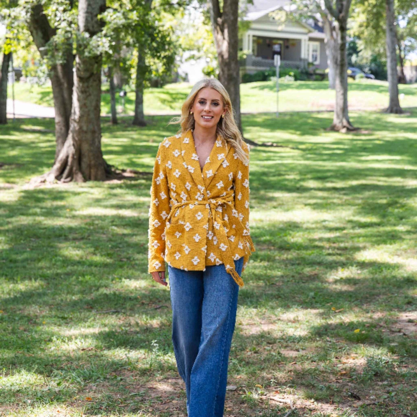 Model walking in park showing fit and belted style of mustard jacket by Modafleur