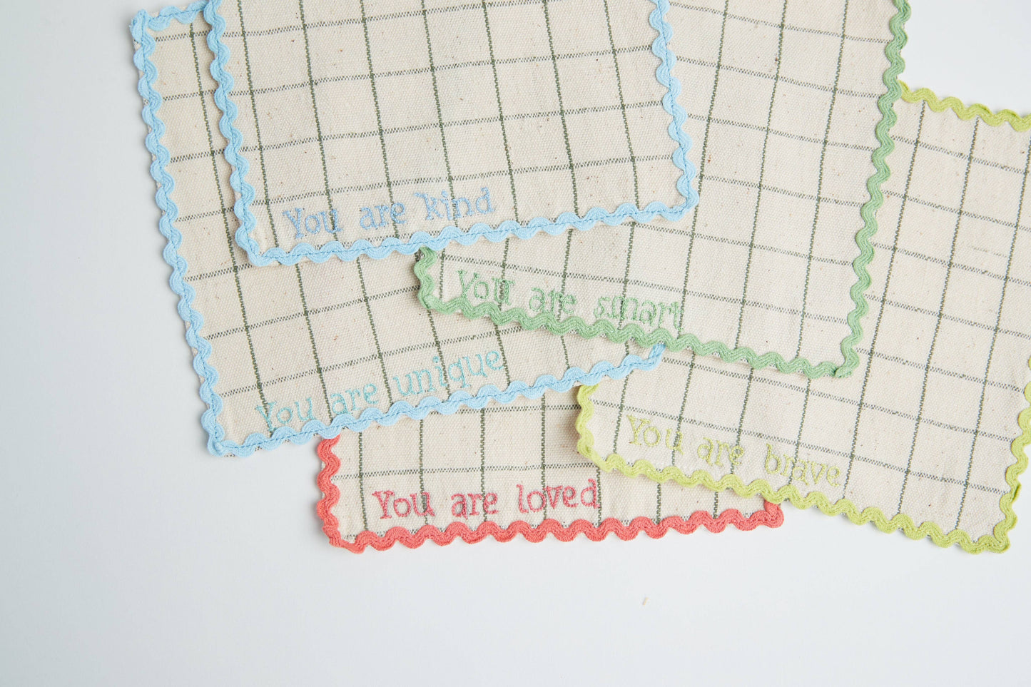 Stack of handwoven lunchbox napkins showing "You Are Loved" embroidery on top napkin in soft, natural tones