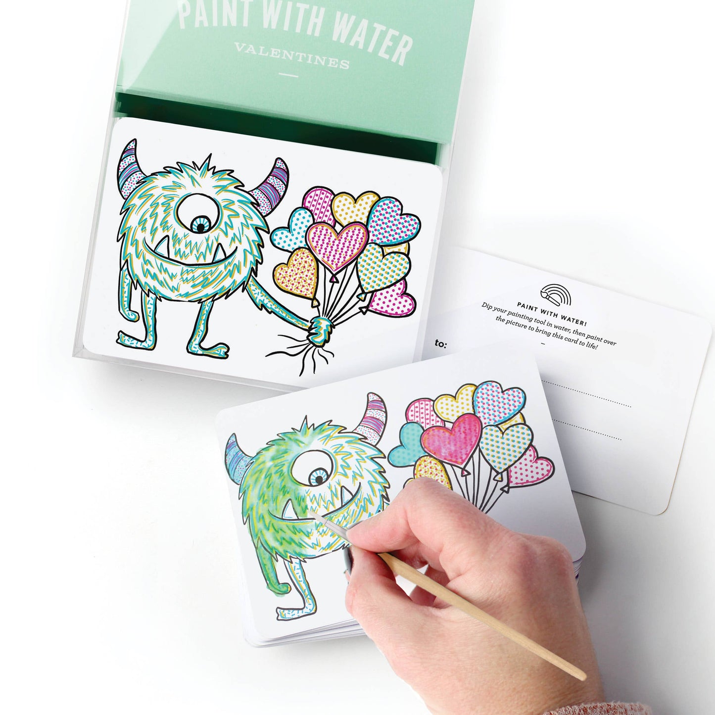 Child using a water painting tool to reveal colors on a monster Valentine card